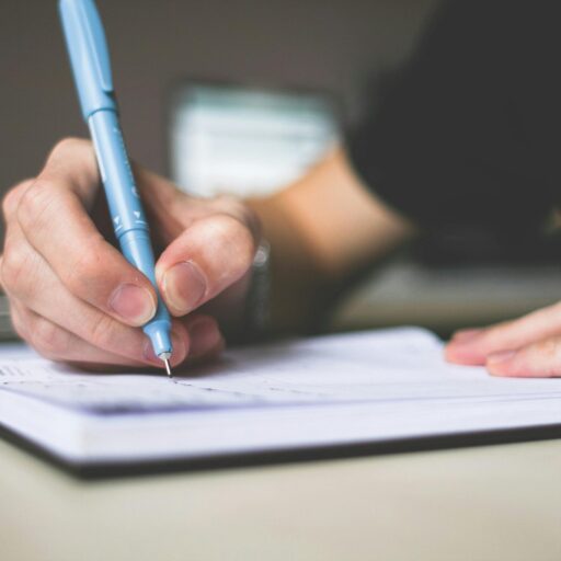 Close-up of hand writing in notebook using a blue pen, focus on creativity.